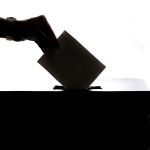 A person casting a vote into a ballot box for board elections