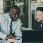 Two business colleagues discussing community strategy at laptop in modern office