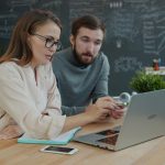 Two specialists sharing business ideas at laptop representing forum moderation and trust level management